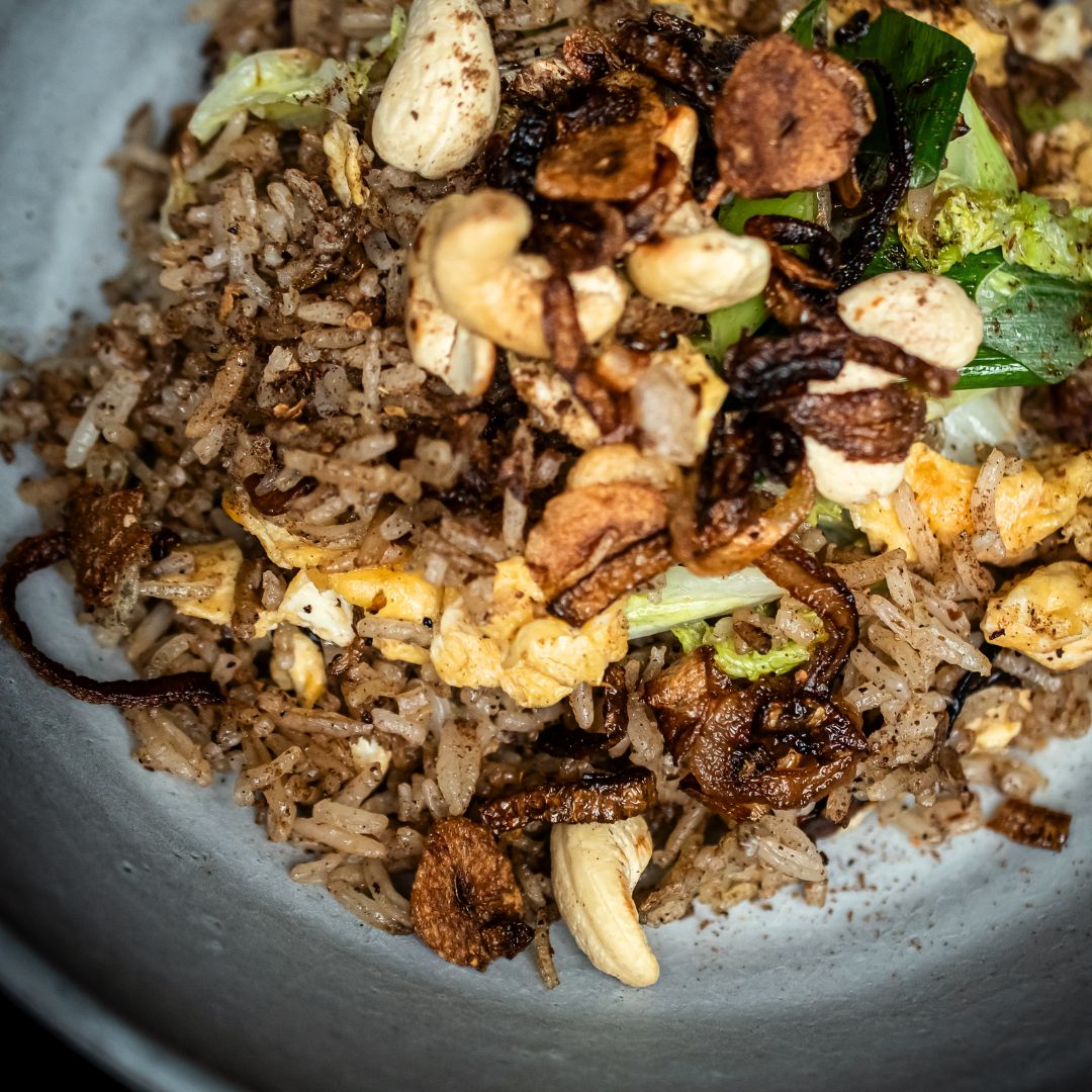 Nahaufnahme eines vollen Tellers mit Crispy Fried Rice mit Five Spice Gewürz aus der Gewürzmühle Rosenheim, Ei, Frühlingszwiebel, Chinakohl, Zwiebeln und Cashewnüssen.