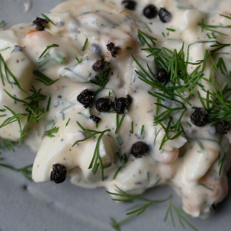 Nahaufnahme eines Eiersalats mit Dill und fermentiertem Kampot Pfeffer der Gewürzmühle Rosenheim. Die schwarzen Pfefferkörner kontrastieren mit der hellen Creme.