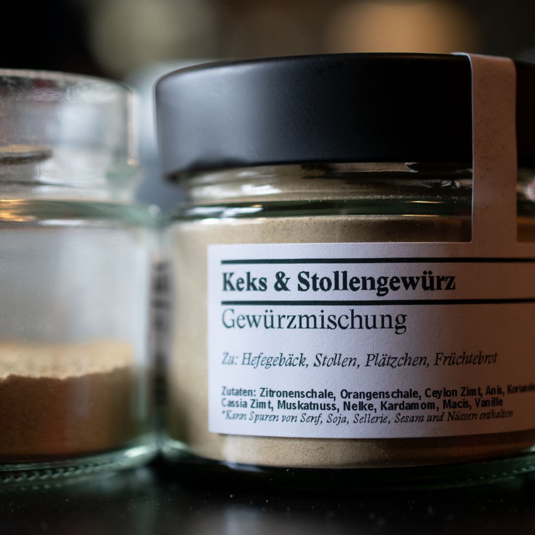 Vier Amaretti Morbidi liegen auf Backpapier und ein geöffnetes Gewürzglas mit Keks- & Stollengewürz steht daneben.