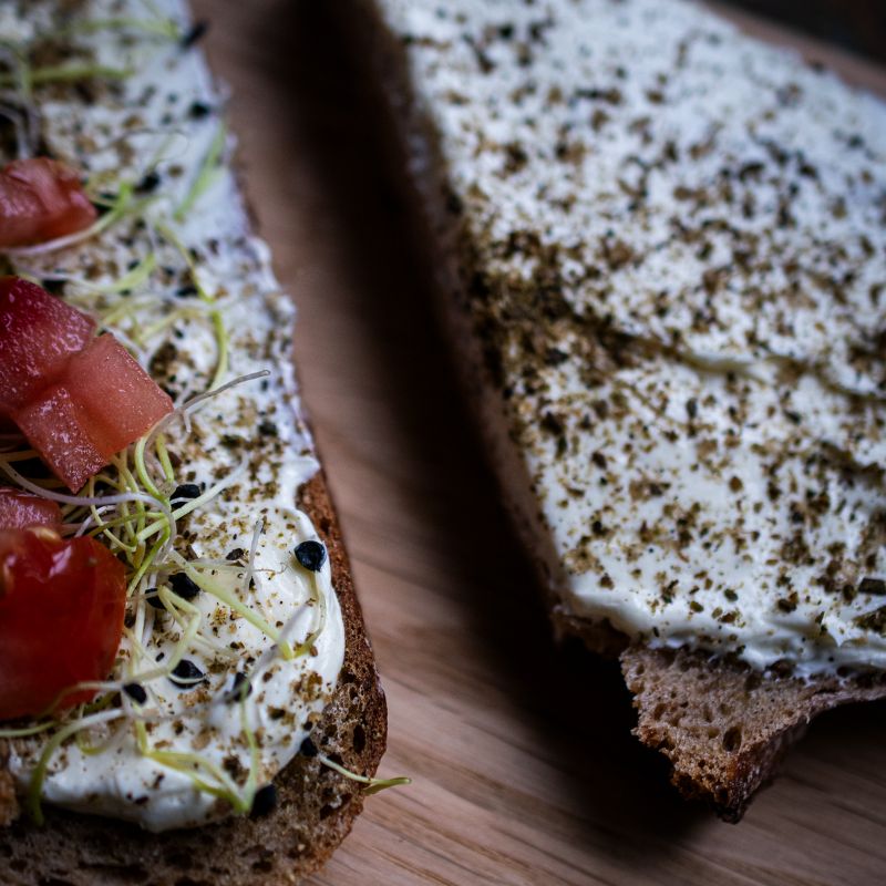 Nahaufnahme einer Brotscheibe mit Butter, Kresse, Tomatenwürfeln und Butterbrotgewürz der Gewürzmühle Rosenheim. Die Gewürzmischung verleiht der Butter eine grünlich-kräuterige Note.
