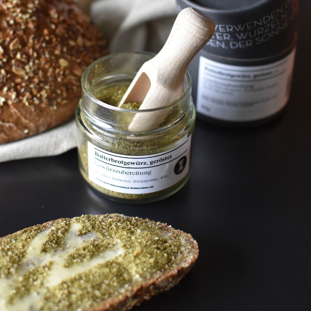 Butterbrotgewürz, geröstet - Gewürzmischung im Glas mit kleiner Holzschaufel und Butterbrot im Vordergrund