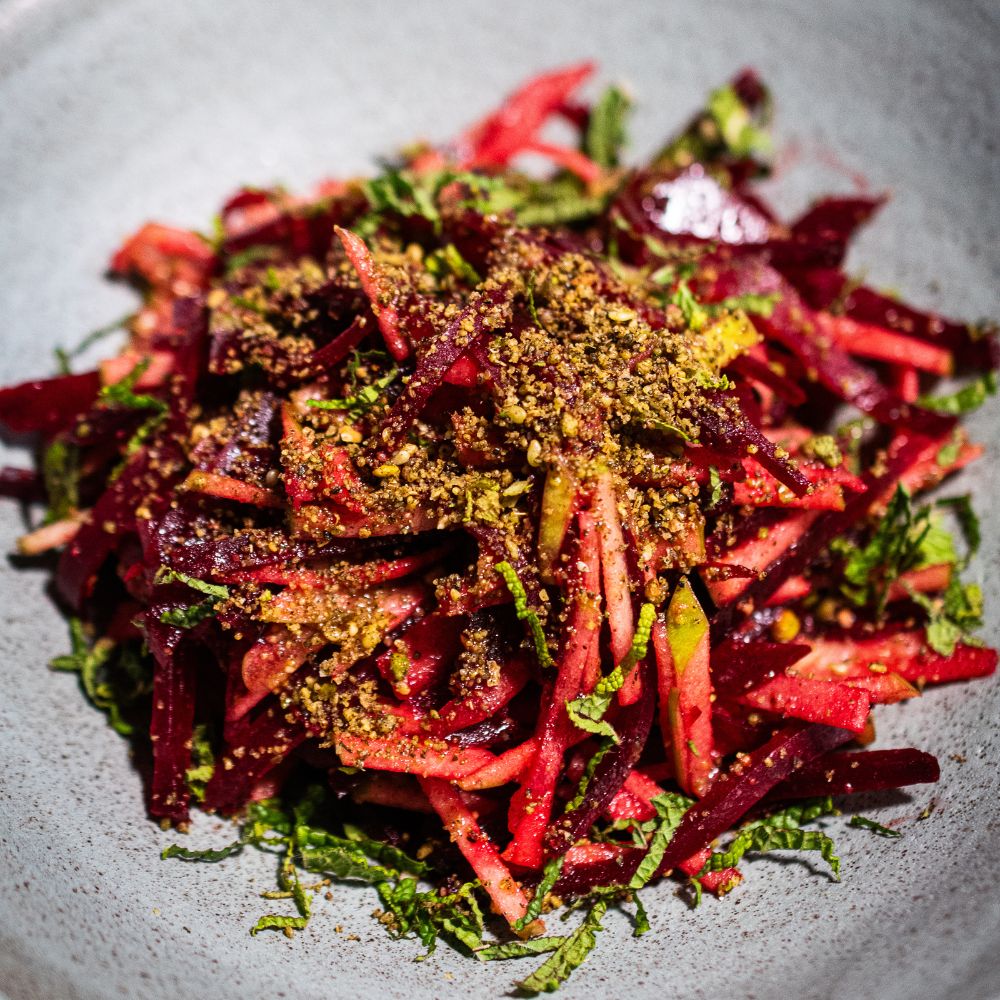 Grauer Teller mit einer Portion Apfel-Rote-Bete-Salat mit etwas Dukkah-Gewürzmischung auf dem Salat und fein geschnittener Minze