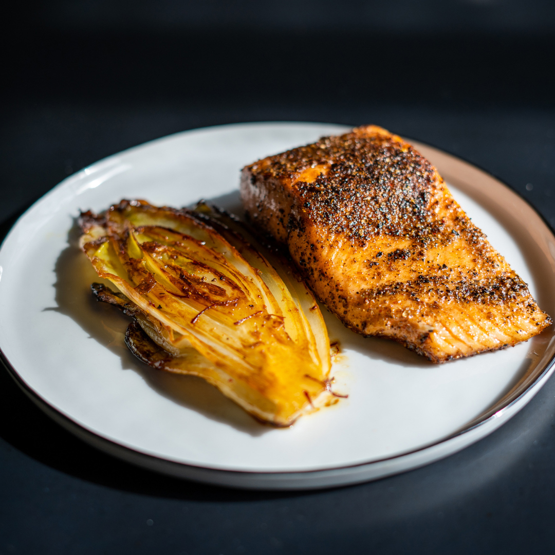 Gegrillter Fisch (Lachs) mit Chicorée auf Teller serviert, dunkler Untergrund