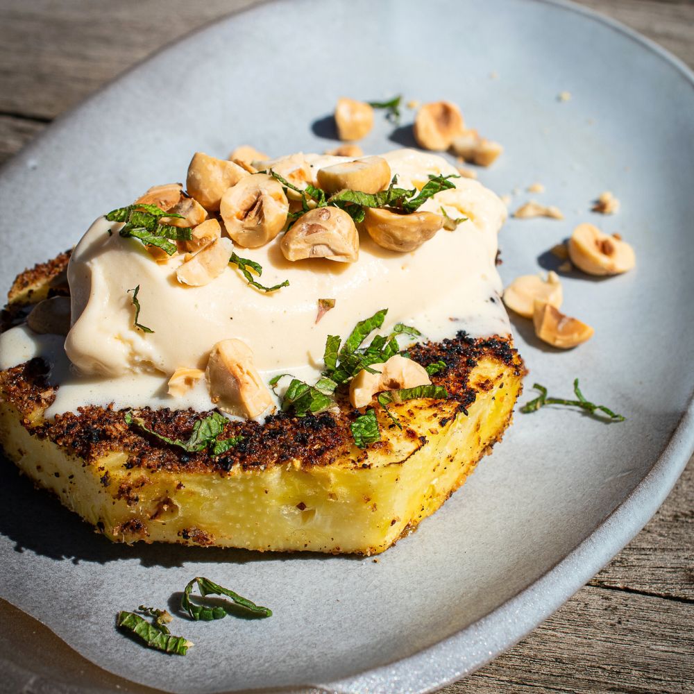 Gegrillte Ananas mit Honeyballs Dessert Rub auf einem Teller serviert mit einer Kugel Vanilleeis und Piemonteser Haselnuessen