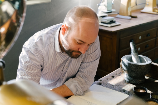 Simon Mendel an einem Tisch im Gewürzladen in Bad Endorf, neben ihm ein Mörser, vor ihm ein aufgeschlagenes Notizbuch.