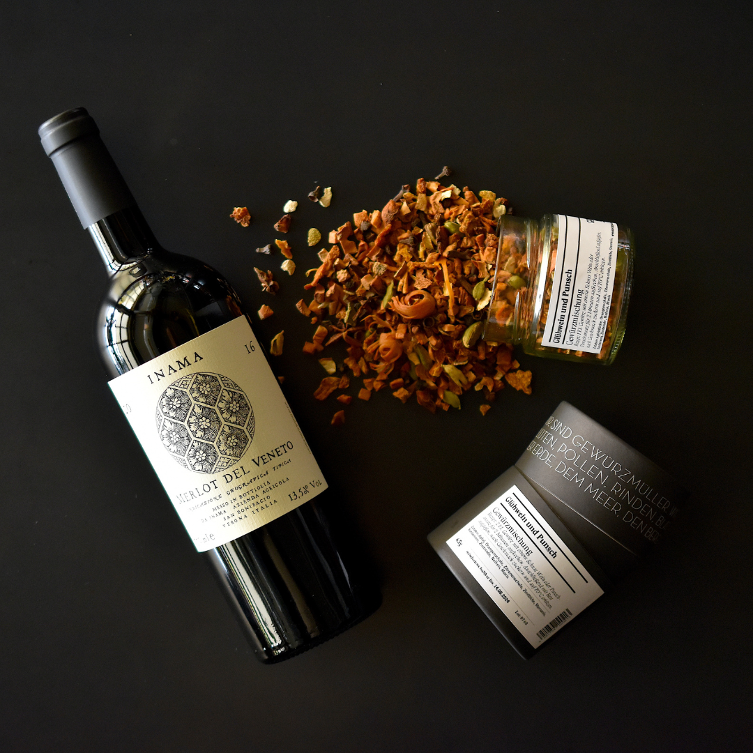 Merlot del Veneto Flasche, Glühwein und Punsch Gewürzmischung im Glas umgekippt und Gewürzdose auf dunklem Untergrund